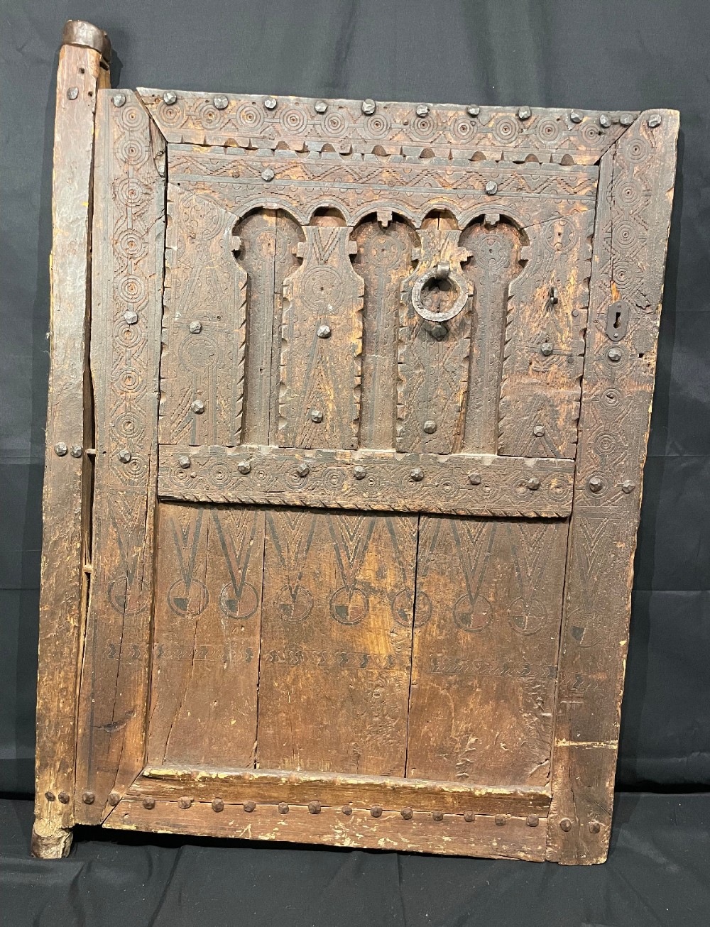 A hand-carved dark timber Amazigh door featuring geometric relief patterns, wrought iron studs, and a circular iron knocker. View II