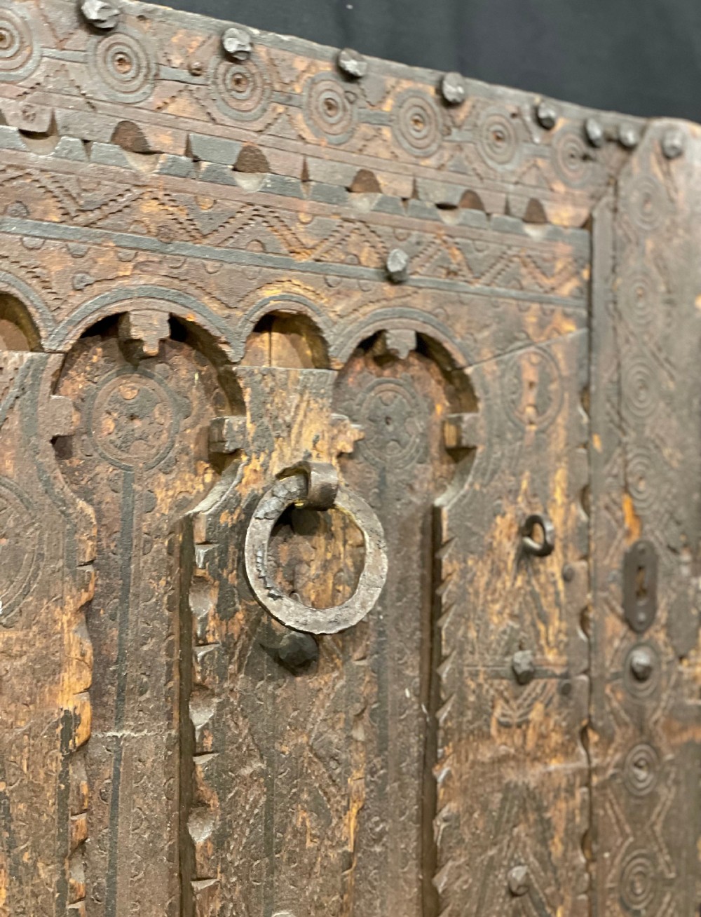 A hand-carved dark timber Amazigh door featuring geometric relief patterns, wrought iron studs, and a circular iron knocker. View III