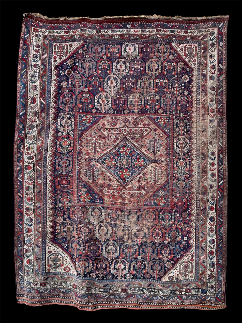 An antique hand-knotted wool carpet displaying a central diamond medallion, geometric borders, and an indigo field filled with intricate tribal motifs.