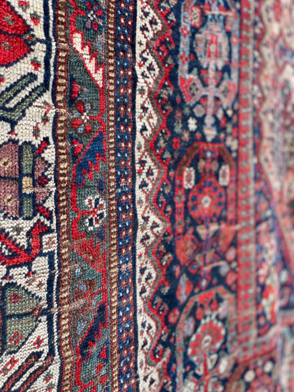 An antique hand-knotted wool carpet displaying a central diamond medallion, geometric borders, and an indigo field filled with intricate tribal motifs. View III