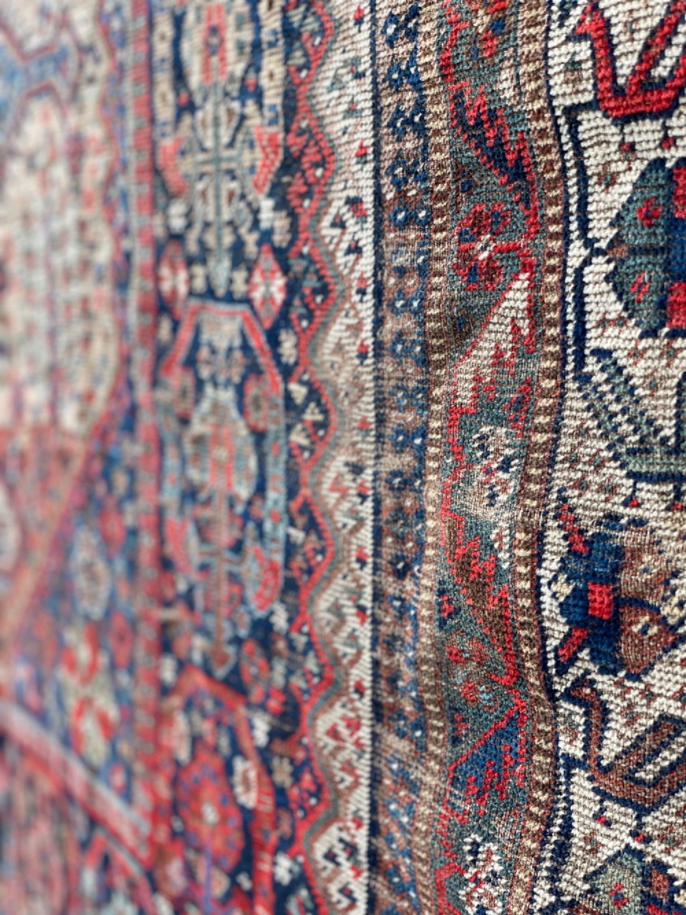 An antique hand-knotted wool carpet displaying a central diamond medallion, geometric borders, and an indigo field filled with intricate tribal motifs. View V