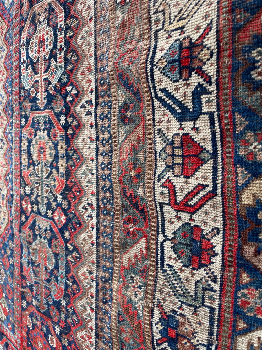 An antique hand-knotted wool carpet displaying a central diamond medallion, geometric borders, and an indigo field filled with intricate tribal motifs. View VI