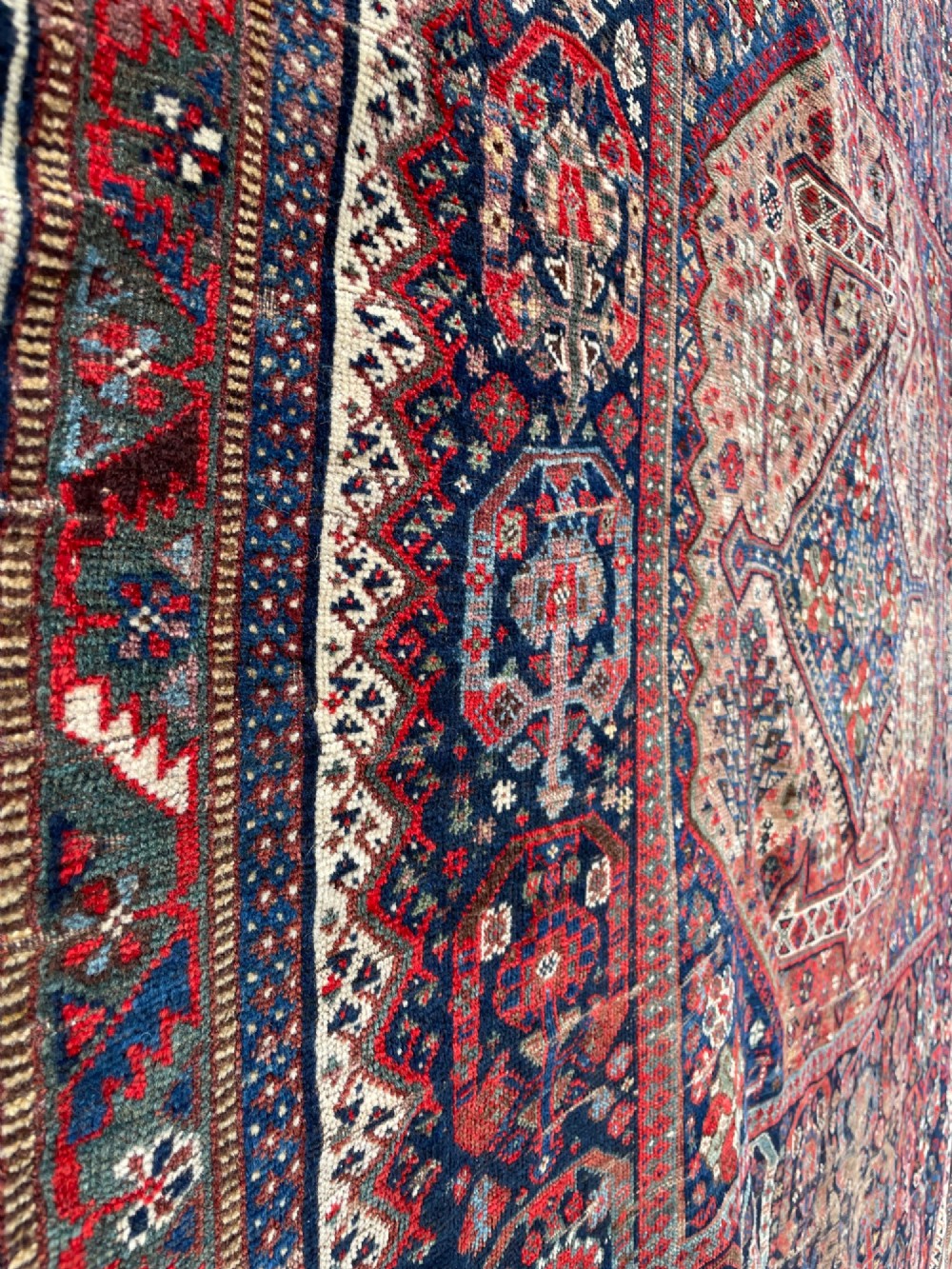 An antique hand-knotted wool carpet displaying a central diamond medallion, geometric borders, and an indigo field filled with intricate tribal motifs. View VII