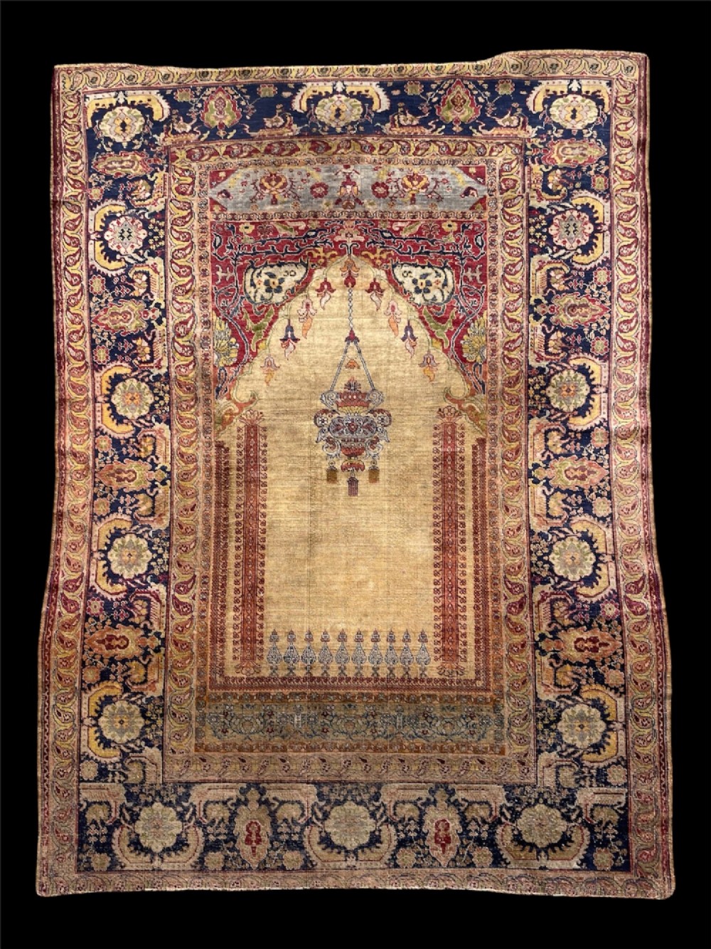 A 19th-century Anatolian silk prayer rug featuring a central gold niche with a hanging lamp motif, enclosed by navy blue and crimson floral borders.