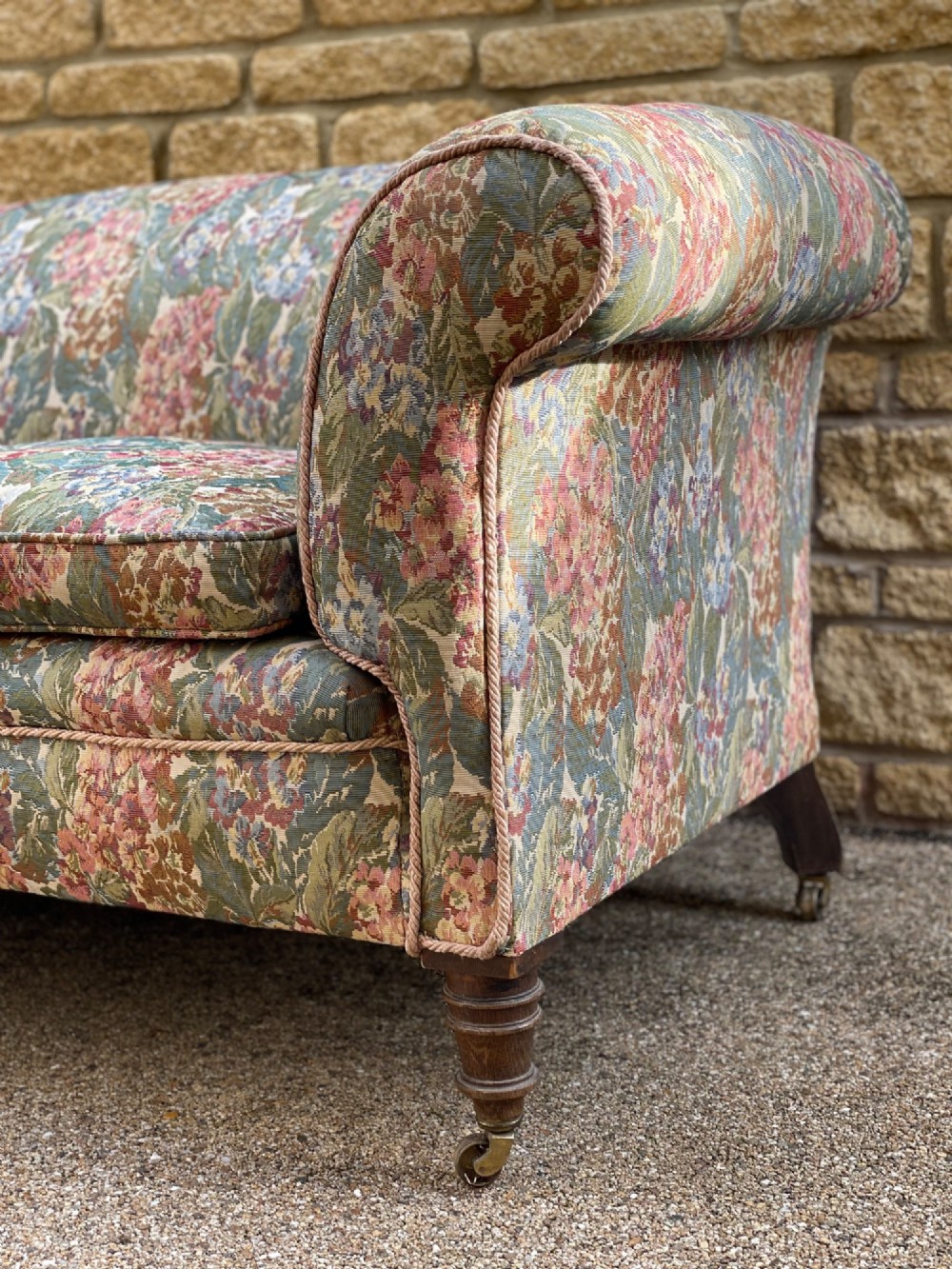 A two-seater Victorian style drop arm sofa upholstered in floral tapestry fabric with turned timber legs on brass castors. View II