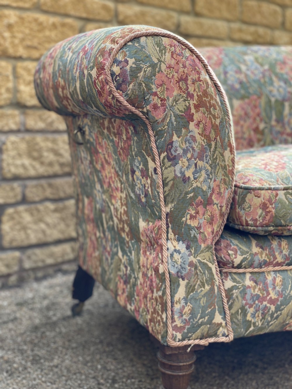 A two-seater Victorian style drop arm sofa upholstered in floral tapestry fabric with turned timber legs on brass castors. View V
