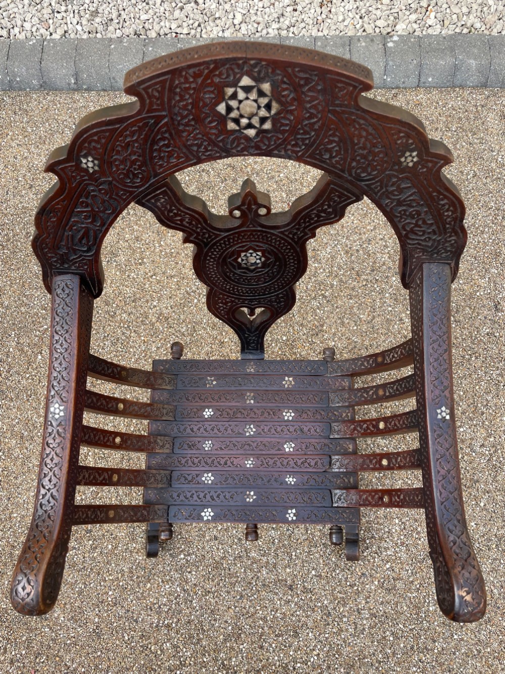 A dark carved wood X-frame armchair featuring intricate Arabic geometric fretwork and inlaid star motifs crafted from iridescent mother of pearl. View VI
