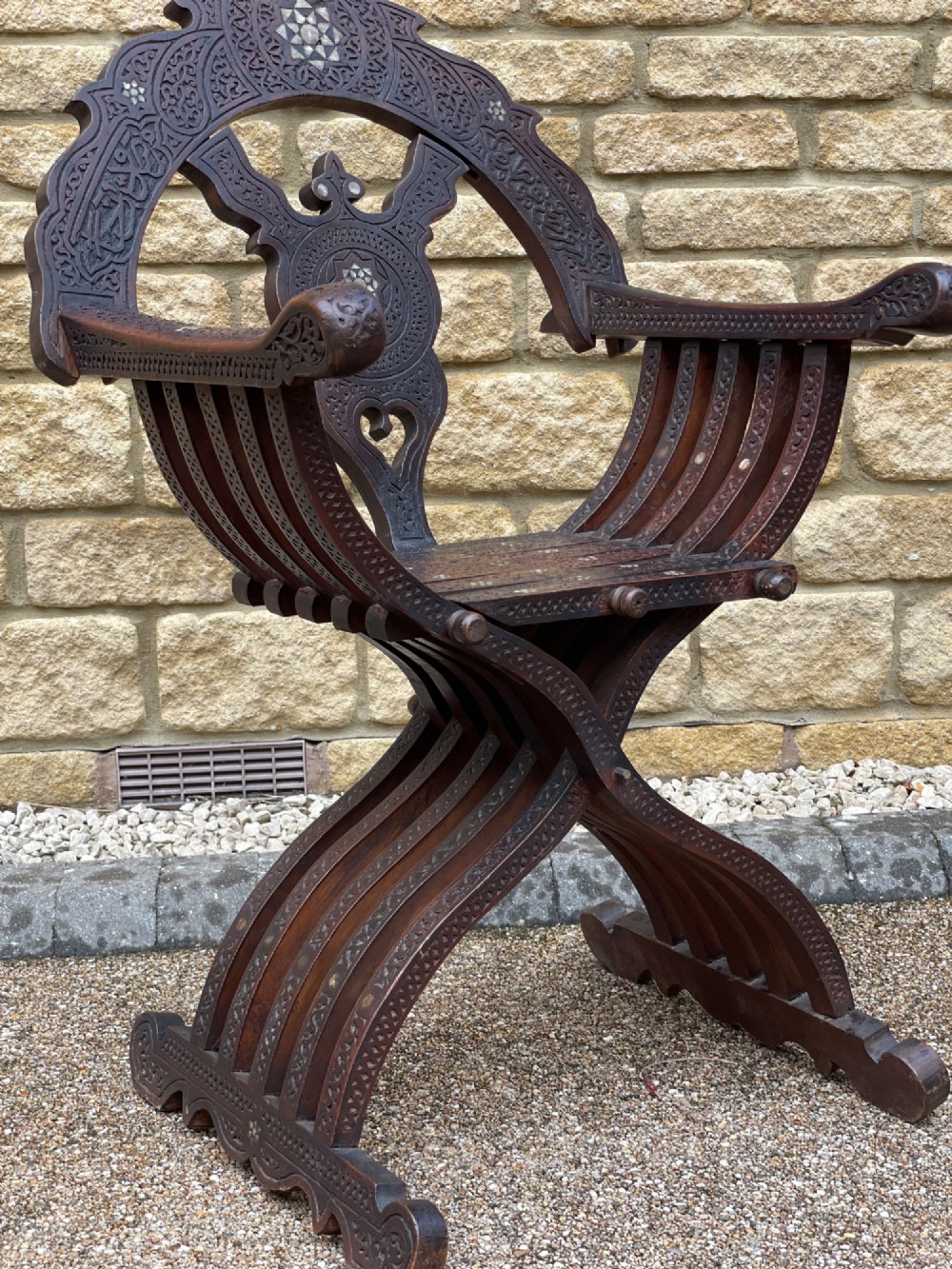 A dark carved wood X-frame armchair featuring intricate Arabic geometric fretwork and inlaid star motifs crafted from iridescent mother of pearl. View VII
