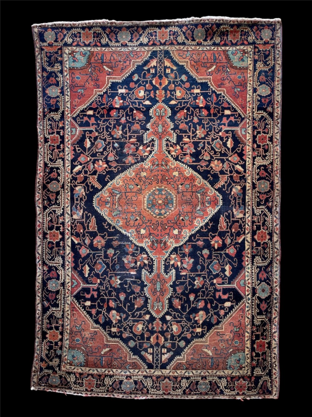 An antique hand-knotted Persian Jozan wool rug featuring a dark navy field filled with floral motifs around a central terracotta red diamond medallion and matching spandrels. View II