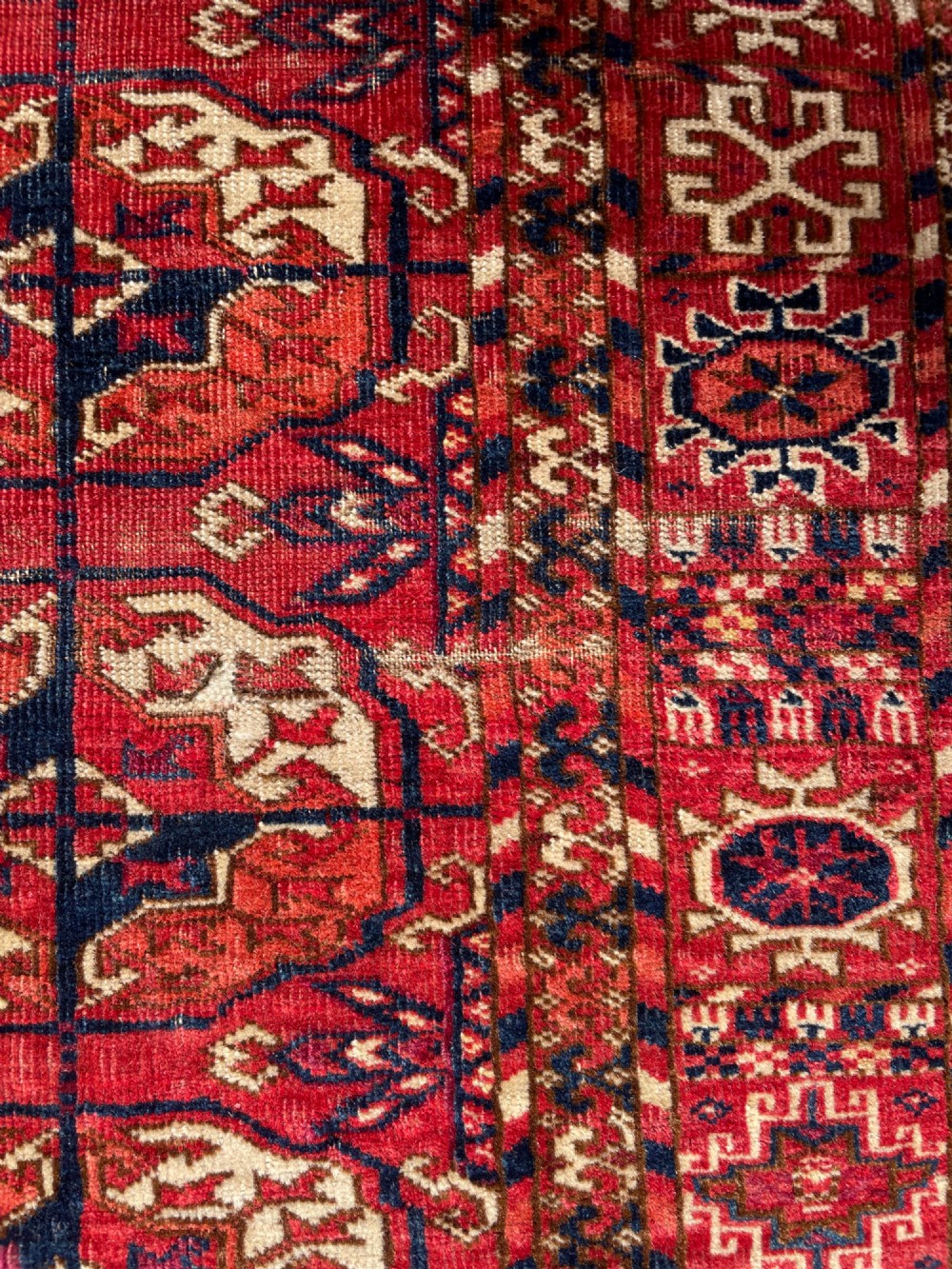 An antique hand-knotted Tekke Turkoman dowry rug featuring repeating octagonal gol motifs in deep red, navy blue, and ivory silk accents. View VI