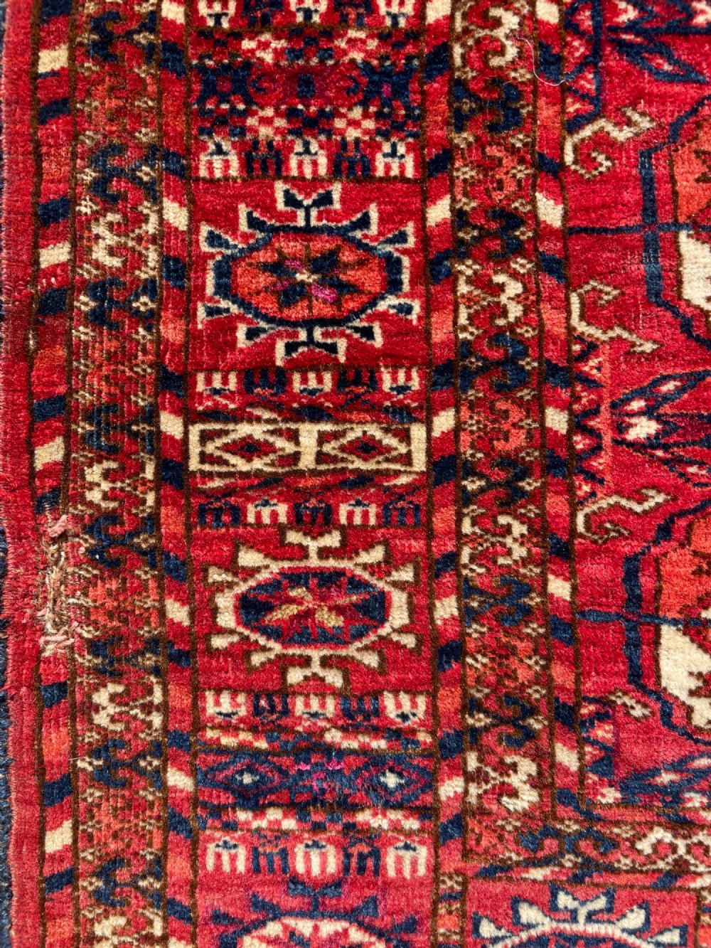 An antique hand-knotted Tekke Turkoman dowry rug featuring repeating octagonal gol motifs in deep red, navy blue, and ivory silk accents. View VII