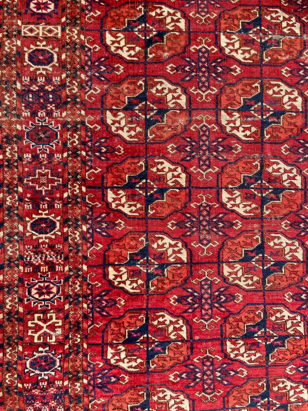 An antique hand-knotted Tekke Turkoman dowry rug featuring repeating octagonal gol motifs in deep red, navy blue, and ivory silk accents. View VIII