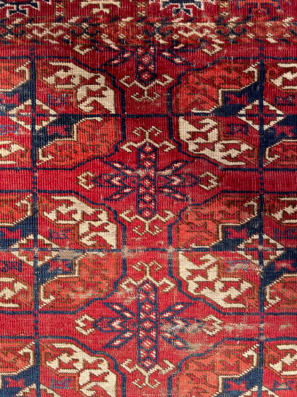 An antique hand-knotted Tekke Turkoman dowry rug featuring repeating octagonal gol motifs in deep red, navy blue, and ivory silk accents. View IX