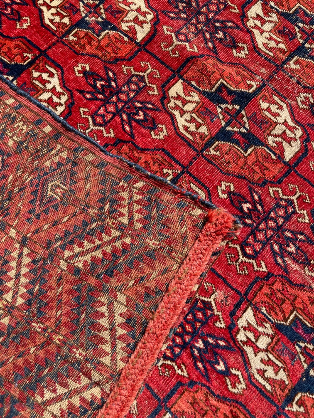 An antique hand-knotted Tekke Turkoman dowry rug featuring repeating octagonal gol motifs in deep red, navy blue, and ivory silk accents. View X