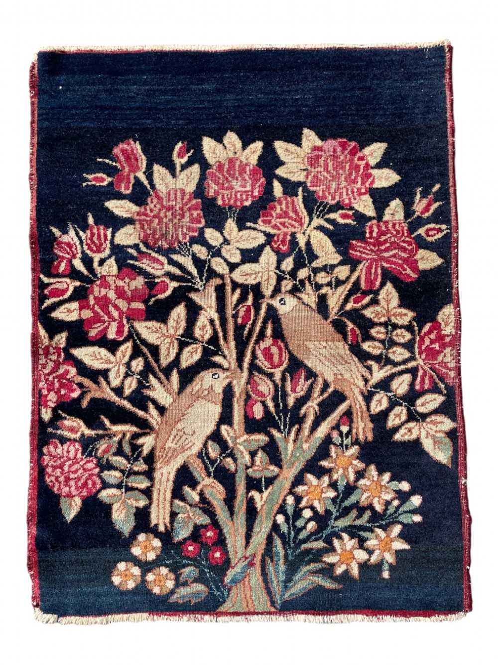 A small antique hand-knotted Kirman rug featuring two birds amongst rose blossoms on a dark navy blue background.