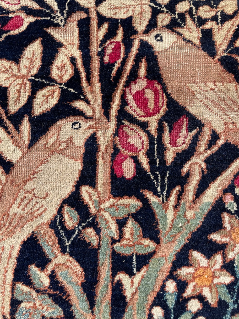 A small antique hand-knotted Kirman rug featuring two birds amongst rose blossoms on a dark navy blue background. View V