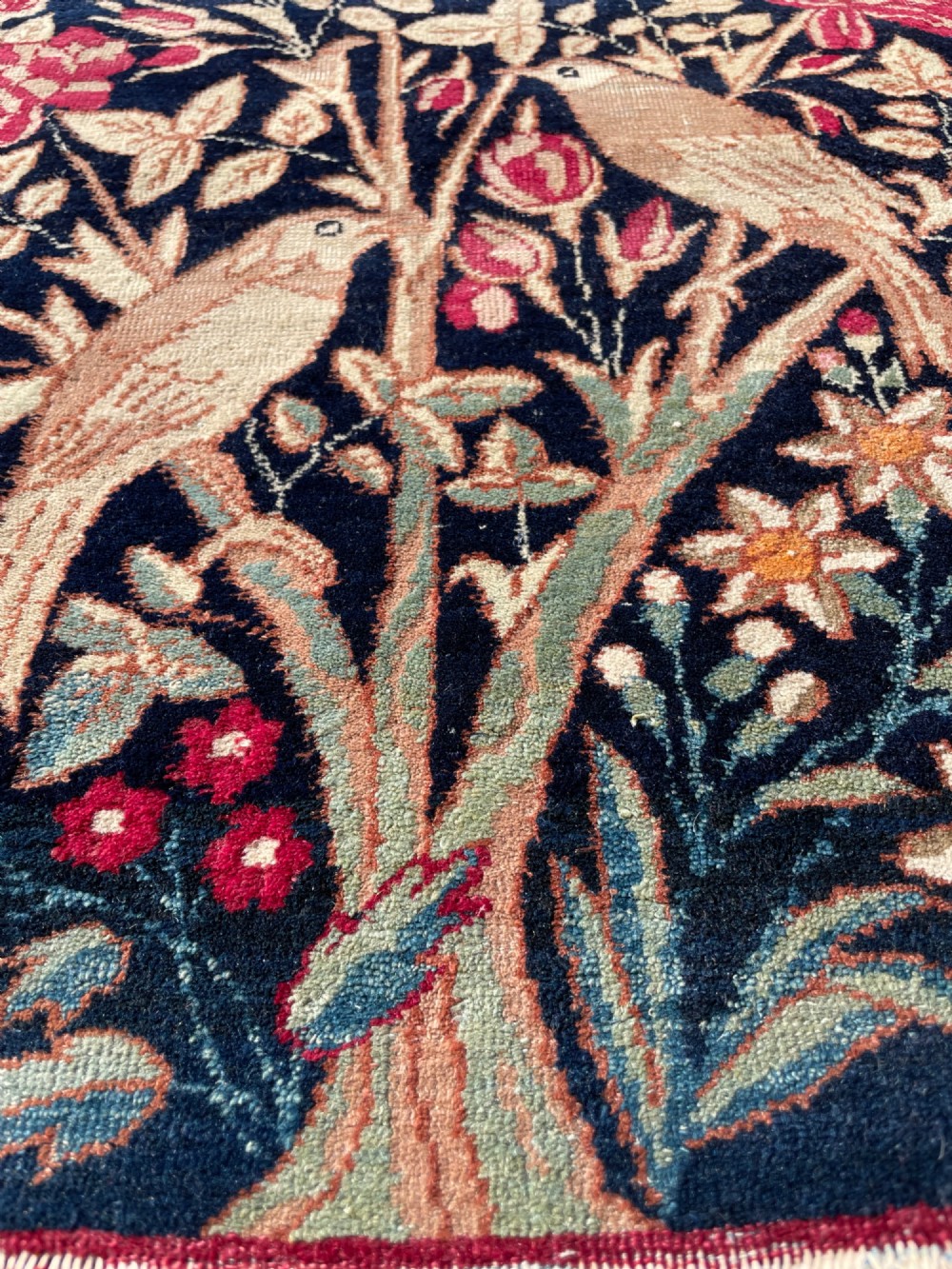 A small antique hand-knotted Kirman rug featuring two birds amongst rose blossoms on a dark navy blue background. View VI