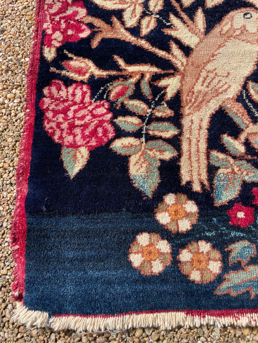 A small antique hand-knotted Kirman rug featuring two birds amongst rose blossoms on a dark navy blue background. View VII