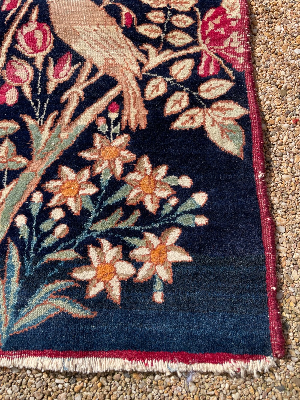 A small antique hand-knotted Kirman rug featuring two birds amongst rose blossoms on a dark navy blue background. View VIII