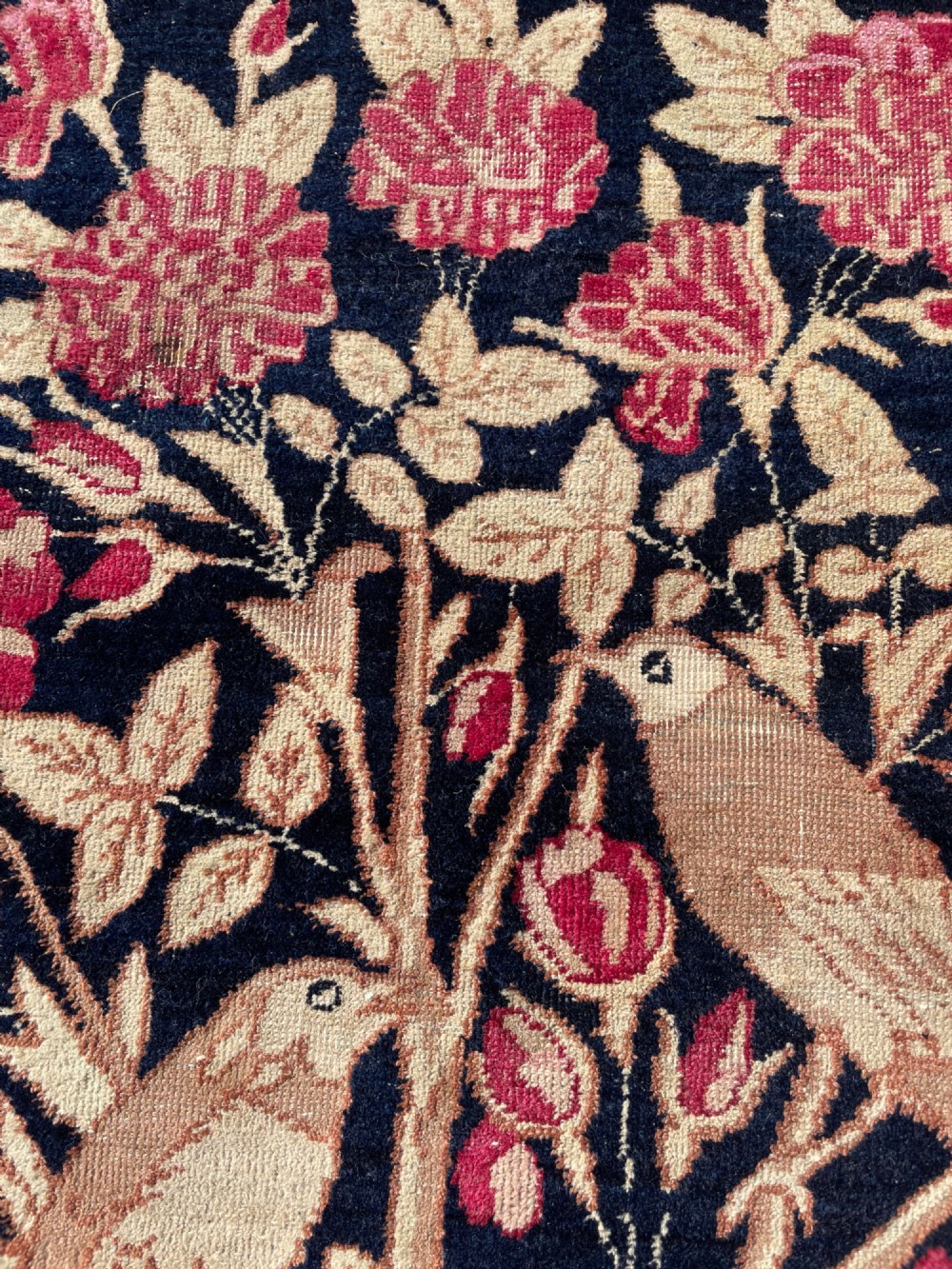 A small antique hand-knotted Kirman rug featuring two birds amongst rose blossoms on a dark navy blue background. View XI
