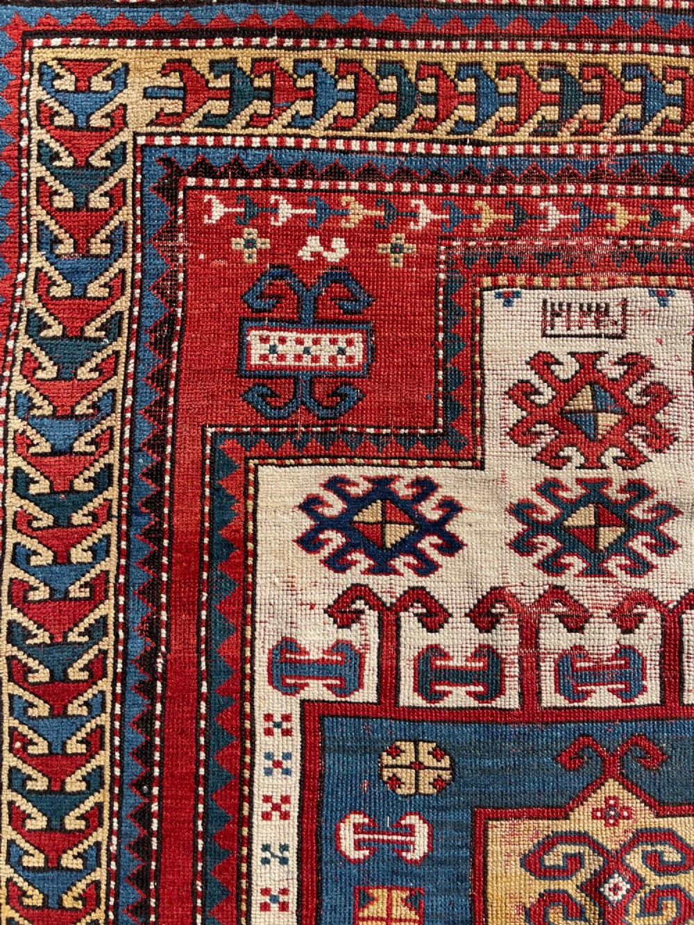 An antique hand-knotted Caucasian Karachov prayer rug featuring a red, ivory, blue, and yellow geometric pattern with a central stepped prayer arch. View XIII