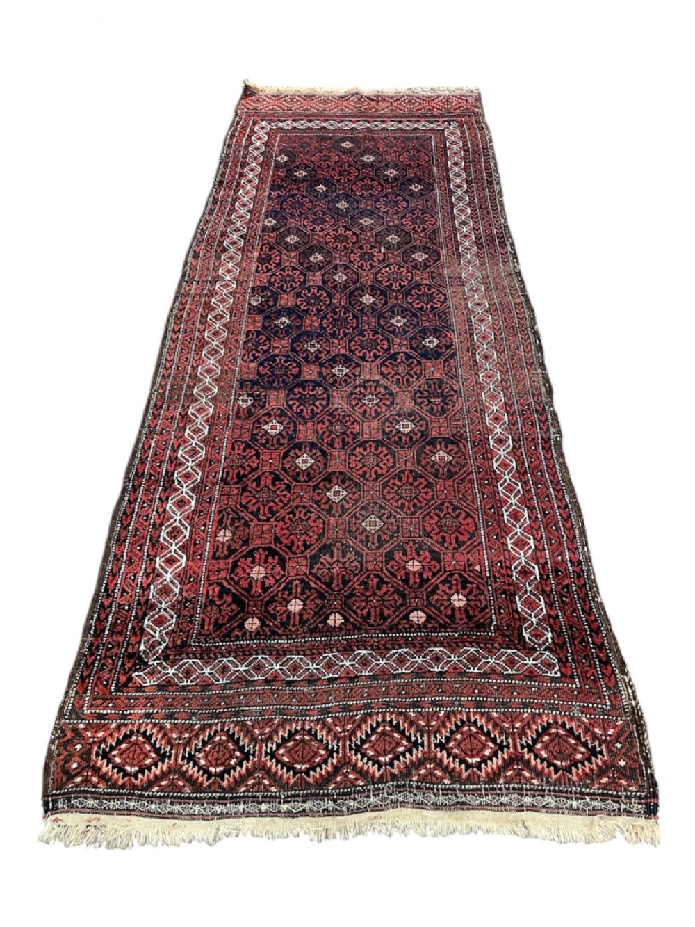 An antique hand-knotted Baluch wool runner rug featuring deep red and navy geometric octagonal motifs with a patterned border and fringed ends.