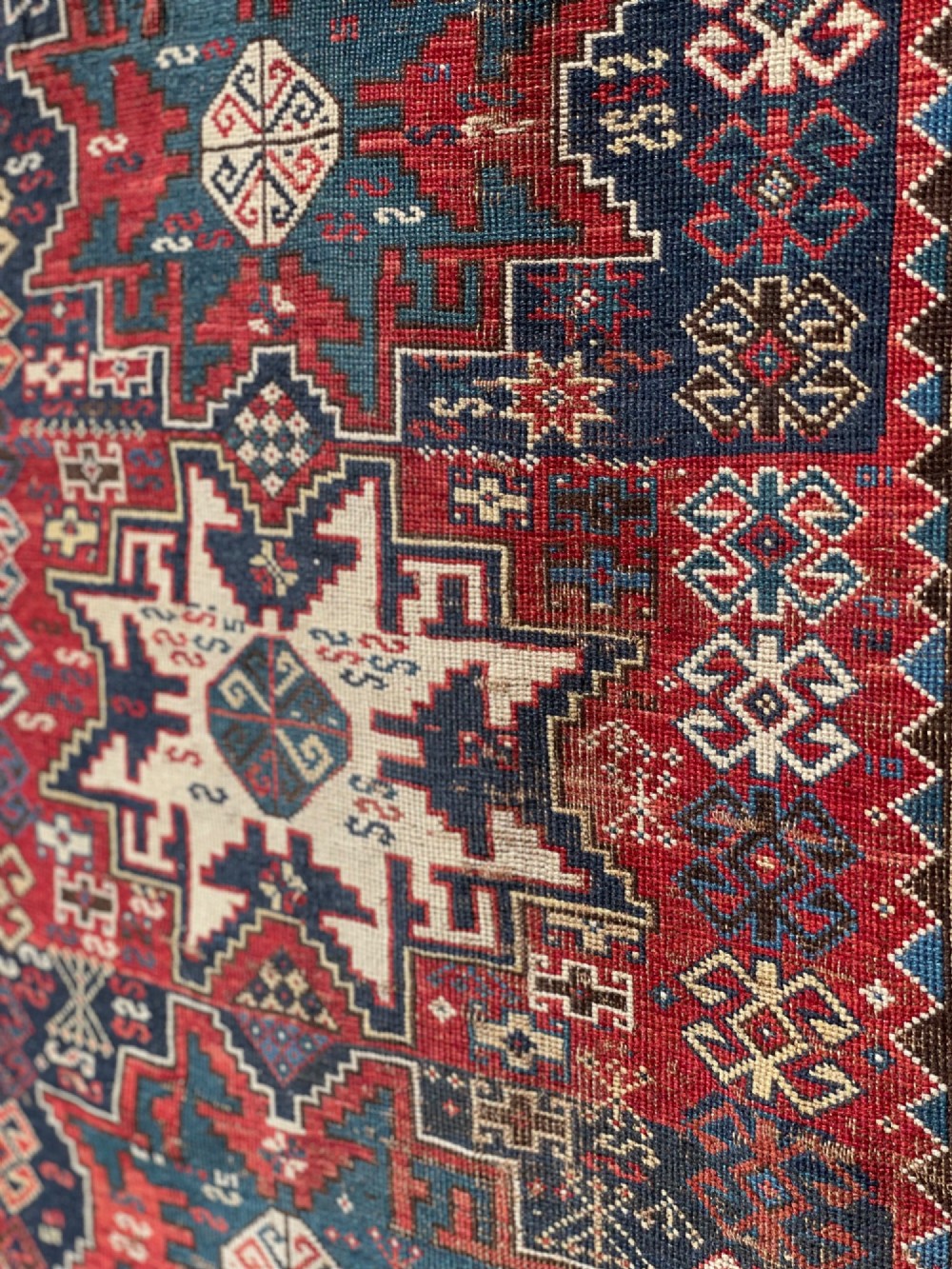 An antique Caucasian hand-knotted wool rug featuring geometric Lezghi star medallions in red, indigo blue, and ivory framed by patterned geometric borders. View II