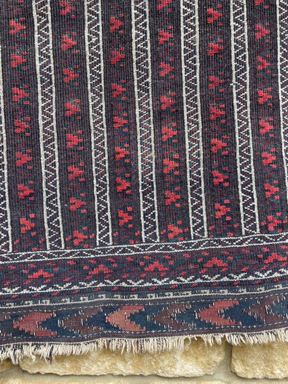 An antique Baluch wool runner rug featuring repeating vertical geometric stripes framed by dark red, navy blue, and ivory patterned borders. View II
