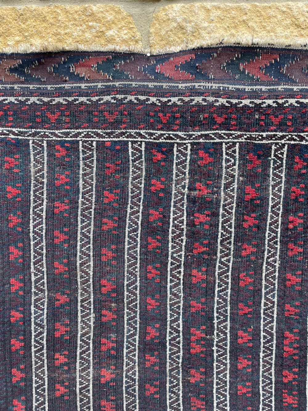 An antique Baluch wool runner rug featuring repeating vertical geometric stripes framed by dark red, navy blue, and ivory patterned borders. View III