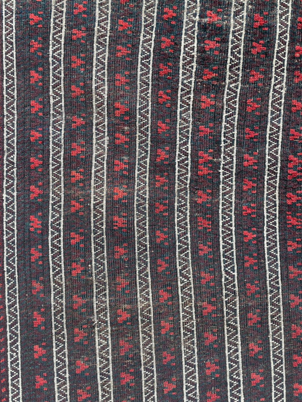 An antique Baluch wool runner rug featuring repeating vertical geometric stripes framed by dark red, navy blue, and ivory patterned borders. View IV