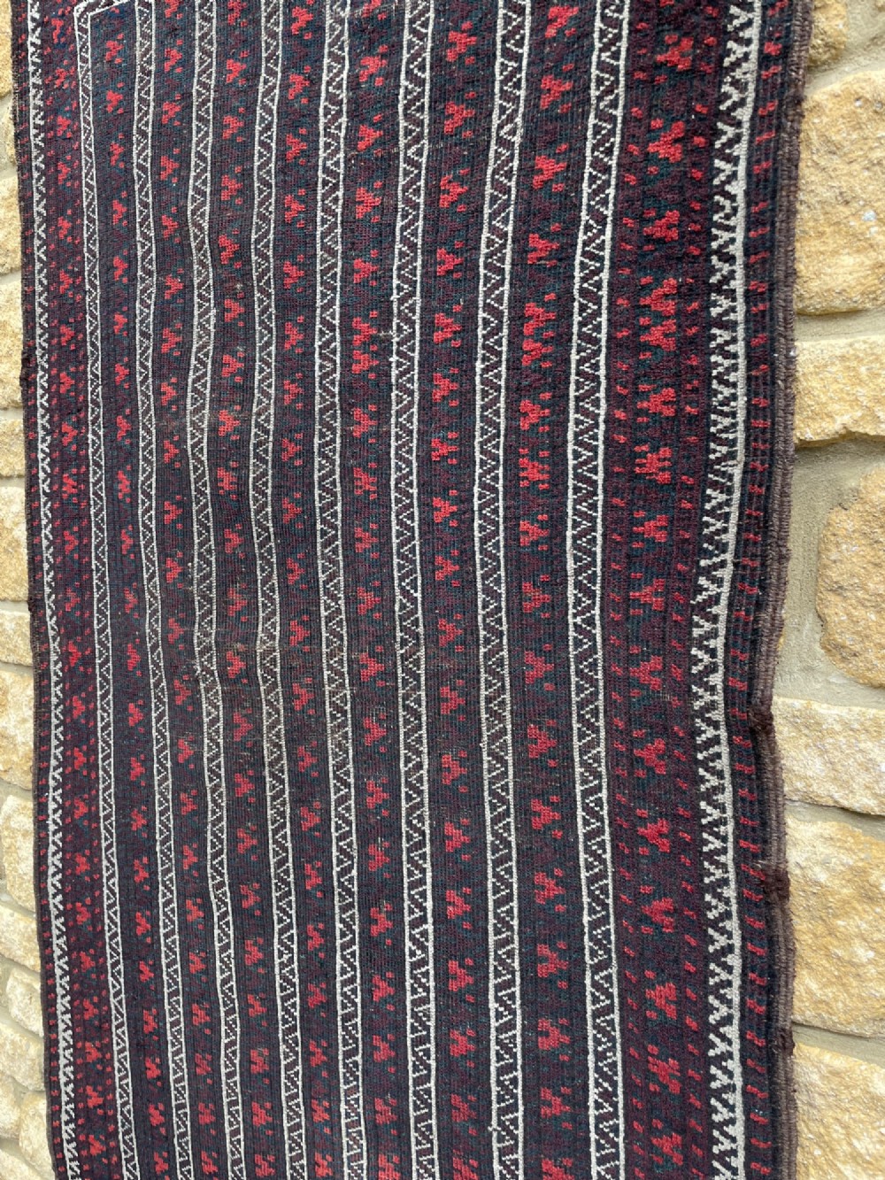 An antique Baluch wool runner rug featuring repeating vertical geometric stripes framed by dark red, navy blue, and ivory patterned borders. View VI