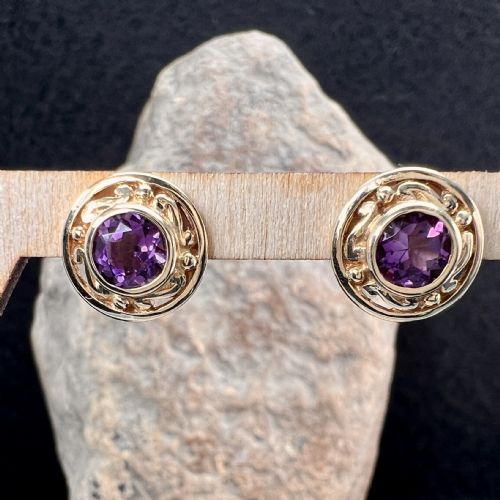 fig 1. A pair of circular 9ct gold stud earrings set with dark purple amethysts and surrounded by patterned gold borders, alongside gold butterfly backs.