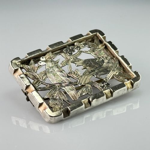 fig 1. An antique rectangular silver openwork brooch depicting two detailed birds surrounded by foliage and berries.