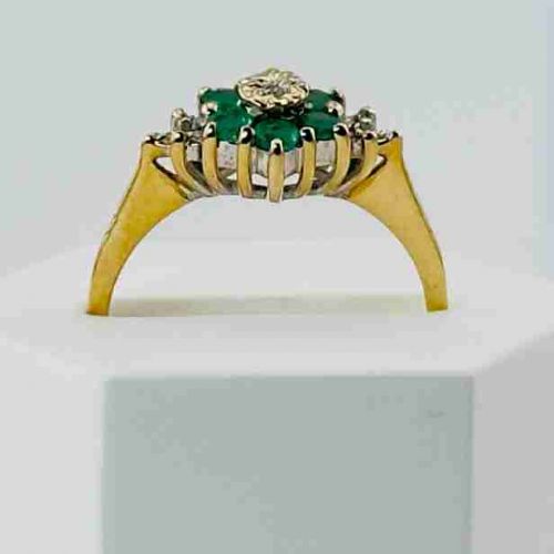 fig 1. A 9ct yellow gold ring featuring a central round diamond surrounded by green emeralds in a floral cluster setting with diamond-set shoulders.