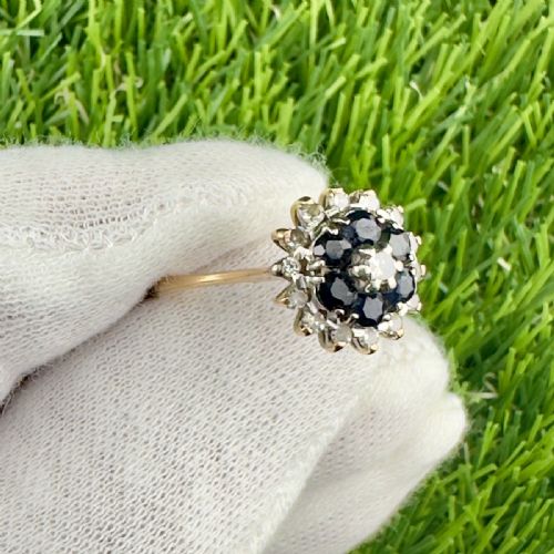 fig 1. An 18ct yellow gold cluster ring set with round deep blue sapphires encircled by small diamond accents in a floral motif.
