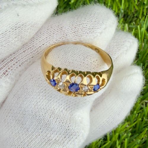 fig 1. An 18ct yellow gold ring set with three blue sapphires and two small diamonds within a carved scrollwork setting.