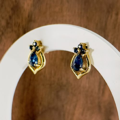 fig 1. A pair of 9ct yellow gold stud earrings featuring pear-cut cabochon blue sapphires set within textured frames and topped with smaller sapphire accents.