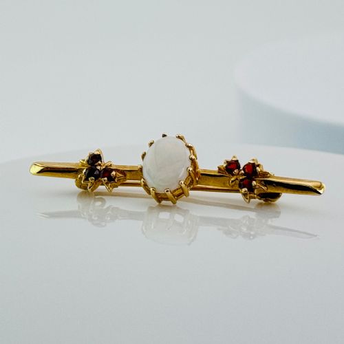 fig 1. A yellow gold bar brooch featuring a central oval cabochon opal flanked by two cluster arrangements of red garnets.