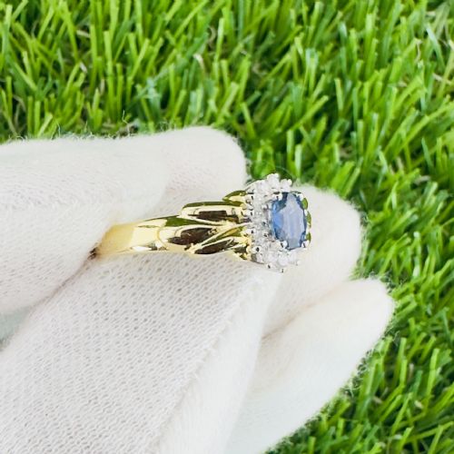 fig 1. An 18ct yellow gold ring featuring a central oval blue sapphire surrounded by a halo of small diamonds and set on fluted shoulders.
