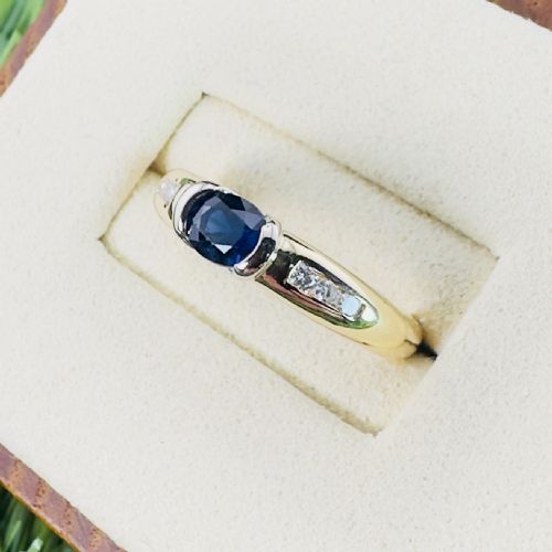 fig 1. An 18ct yellow gold band ring with a central oval dark blue sapphire and small accent diamonds set into each shoulder.