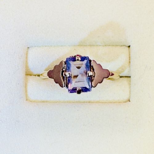 fig 1. A 9ct gold Art Deco solitaire ring featuring a rectangular emerald-cut purple sapphire set with four double claw corner mounts and stepped shoulder details.