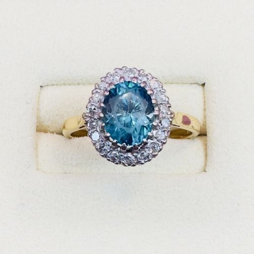 fig 1. An Art Deco cluster ring featuring a central oval blue zircon gemstone surrounded by a halo of round diamonds set on an 18ct yellow gold band.