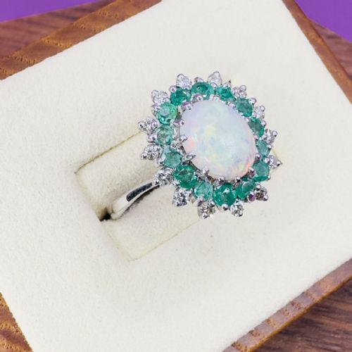 fig 1. An 18ct white gold cocktail ring featuring a central oval cabochon opal encircled by a dual halo of round emeralds and accent diamonds.