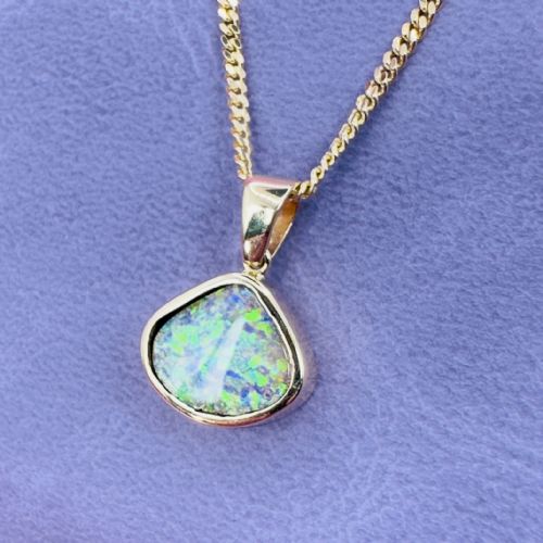 fig 1. A 9ct yellow gold pendant featuring a freeform triangular boulder opal with blue and green play-of-colour attached to a gold curb chain.