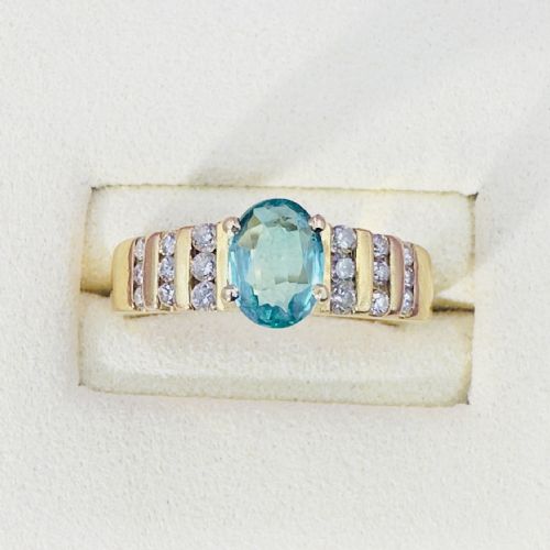 fig 1. An 18ct yellow gold ring featuring a central oval-cut light green gemstone flanked by channel-set diamonds along a ridged band.