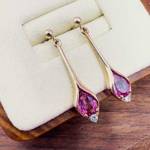 fig 1. A pair of 9ct yellow gold drop earrings featuring sleek elongated mounts holding pear-cut pink topaz gemstones with small white topaz accents at the base.