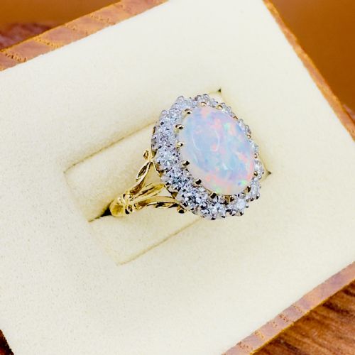 fig 1. An 18ct gold ring featuring a central oval cabochon opal framed by a halo of brilliant-cut diamonds with carved shoulders.