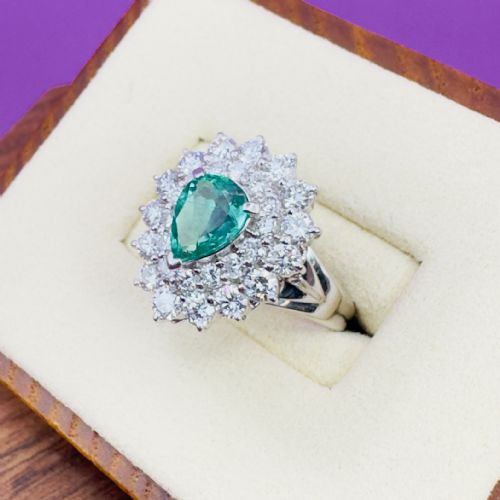 fig 1. A platinum cluster ring set with a pear cut green emerald surrounded by a double halo of round diamonds.