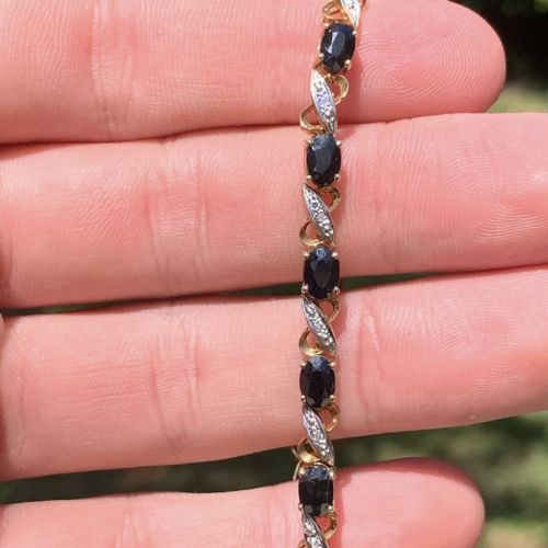 fig 1. A 9ct yellow gold link bracelet set with oval-cut dark blue sapphires and accent diamond links, worn on a wrist.