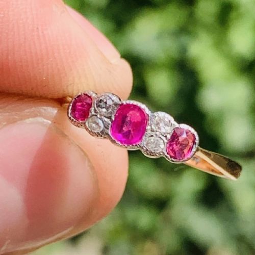 An 18ct yellow gold ring featuring three oval pinkish-red rubies interspersed with pairs of small round old-cut diamonds in a platinum setting. View IV